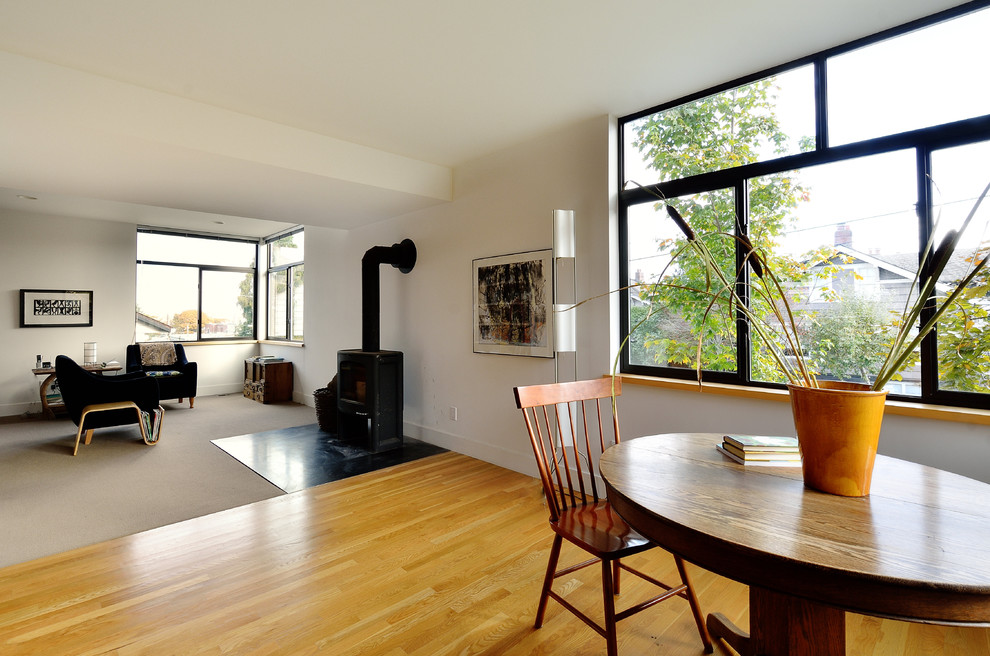 This is an example of a large modern open plan dining in Seattle with white walls, a wood stove, dark hardwood floors, brown floor and a metal fireplace surround.