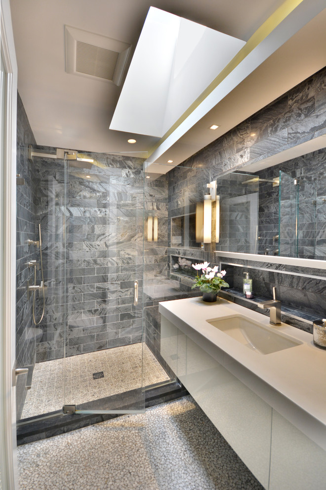 Photo of a mid-sized modern master bathroom in New York with flat-panel cabinets, white cabinets, an alcove shower, a one-piece toilet, grey walls, pebble tile floors, an undermount sink, white floor, a hinged shower door, gray tile, marble and glass benchtops.