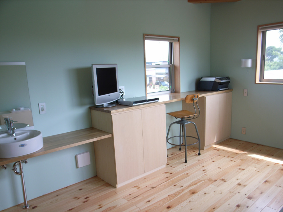 Modelo de despacho beige nórdico de tamaño medio con paredes verdes, suelo de madera clara, escritorio empotrado, suelo beige, madera y machihembrado