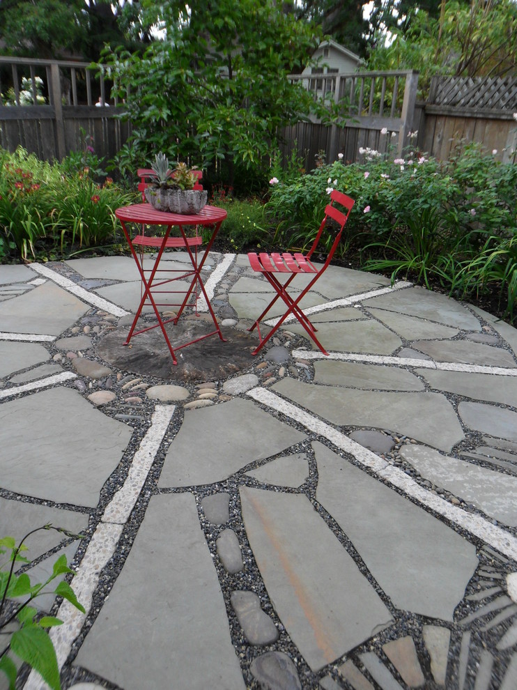 Small eclectic backyard full sun garden in Portland with natural stone pavers for summer.