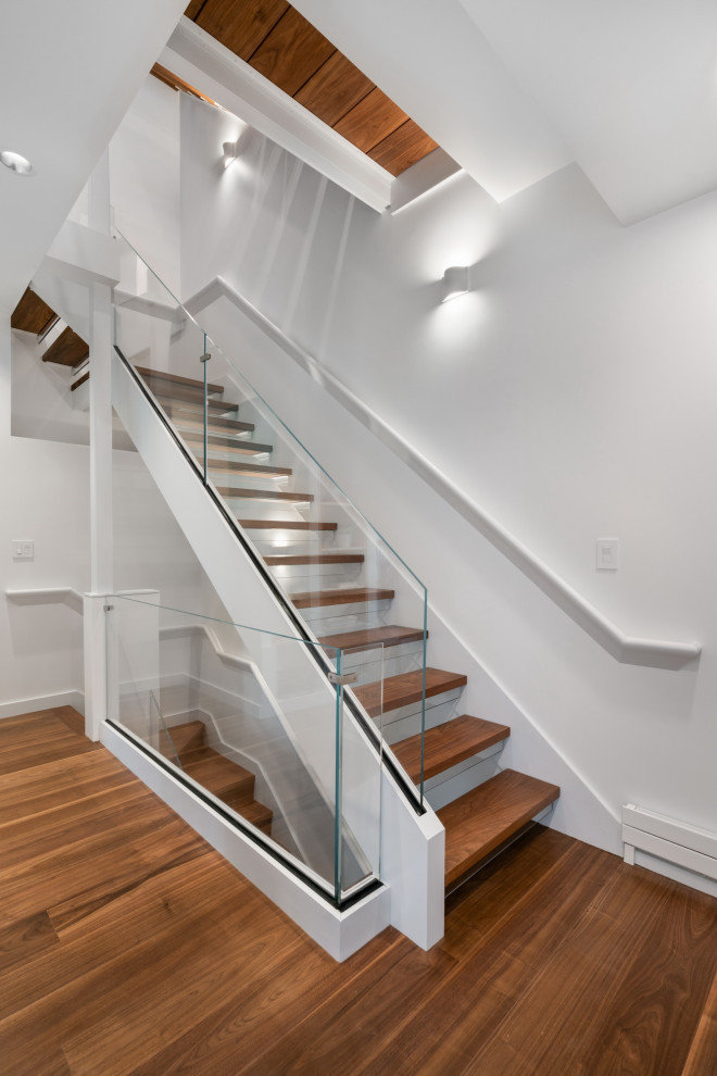 This is an example of a small modern wood floating glass railing staircase in Boston with glass risers.