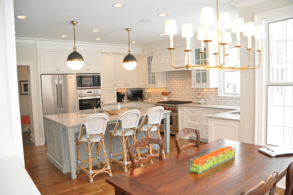 Open concept kitchen - large transitional l-shaped medium tone wood floor and brown floor open concept kitchen idea in Cleveland with an undermount sink, recessed-panel cabinets, white cabinets, marble countertops, white backsplash, subway tile backsplash, stainless steel appliances, an island and white countertops