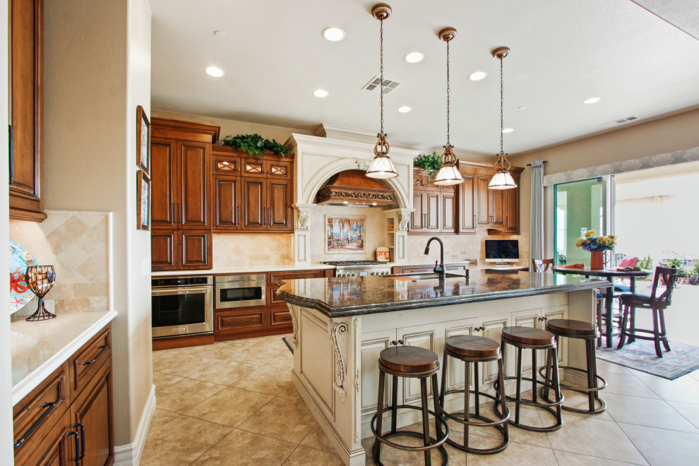 Example of a large tuscan l-shaped beige floor eat-in kitchen design in Los Angeles with an island, an undermount sink, raised-panel cabinets, dark wood cabinets, beige backsplash, stainless steel appliances and beige countertops