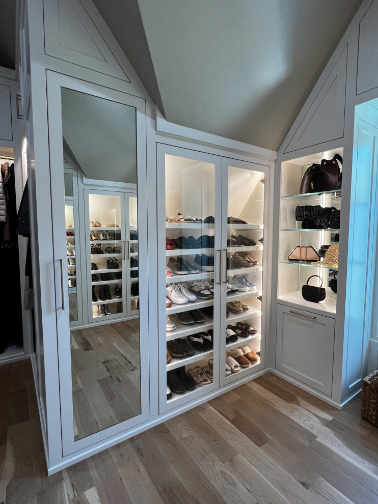 This is an example of a large gender-neutral walk-in wardrobe in Dallas with white cabinets, light hardwood floors, beige floor and vaulted.