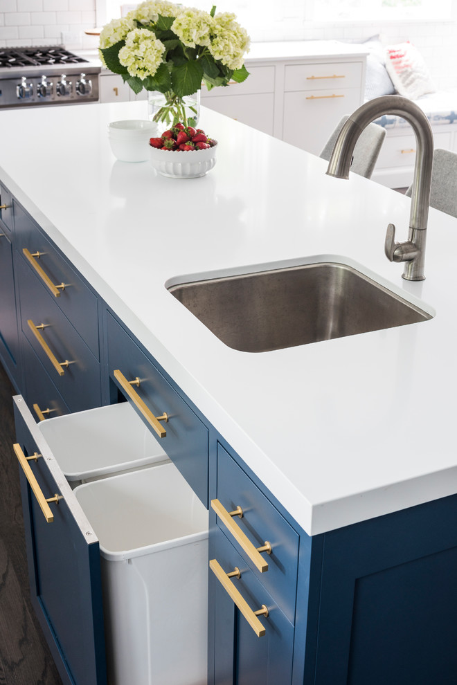Example of a large transitional l-shaped medium tone wood floor and brown floor eat-in kitchen design in New York with a double-bowl sink, shaker cabinets, blue cabinets, quartz countertops, white backsplash, ceramic backsplash, stainless steel appliances and an island