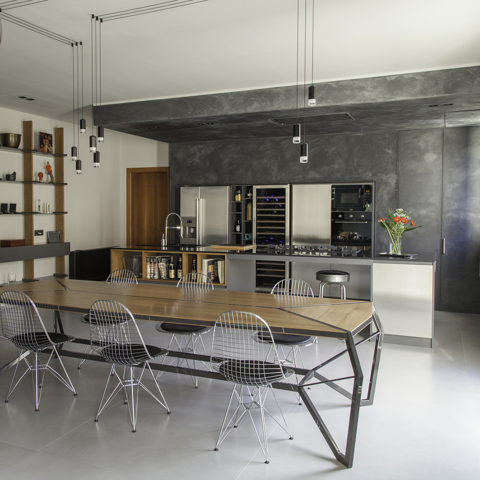 Photo of a large industrial eat-in kitchen in Other with quartz benchtops, stainless steel appliances, porcelain floors, with island, grey floor, black benchtop, flat-panel cabinets and distressed cabinets.