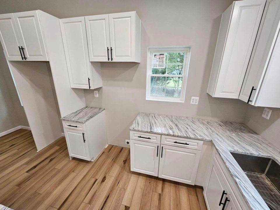 Example of a mid-sized transitional l-shaped medium tone wood floor and brown floor kitchen design in DC Metro with an undermount sink, raised-panel cabinets, white cabinets, quartz countertops, stainless steel appliances and multicolored countertops