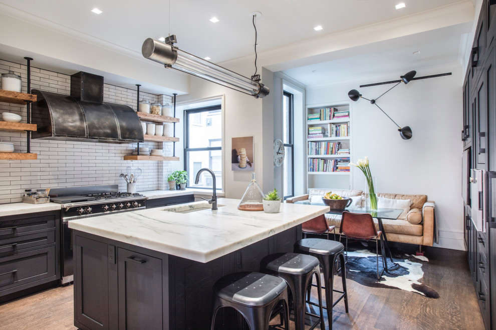 Photo of an industrial galley kitchen in New York with an undermount sink, shaker cabinets, black cabinets, white splashback, black appliances, dark hardwood floors, with island and brown floor.