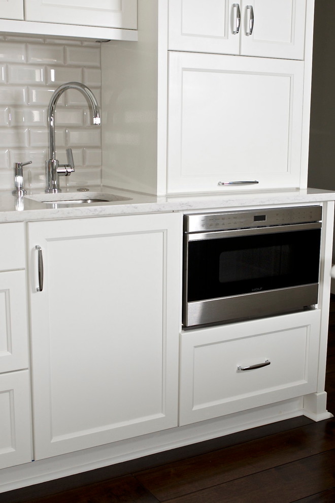 Example of a mid-sized transitional u-shaped dark wood floor eat-in kitchen design in Atlanta with an undermount sink, glass-front cabinets, white cabinets, quartz countertops, white backsplash, subway tile backsplash, paneled appliances and an island