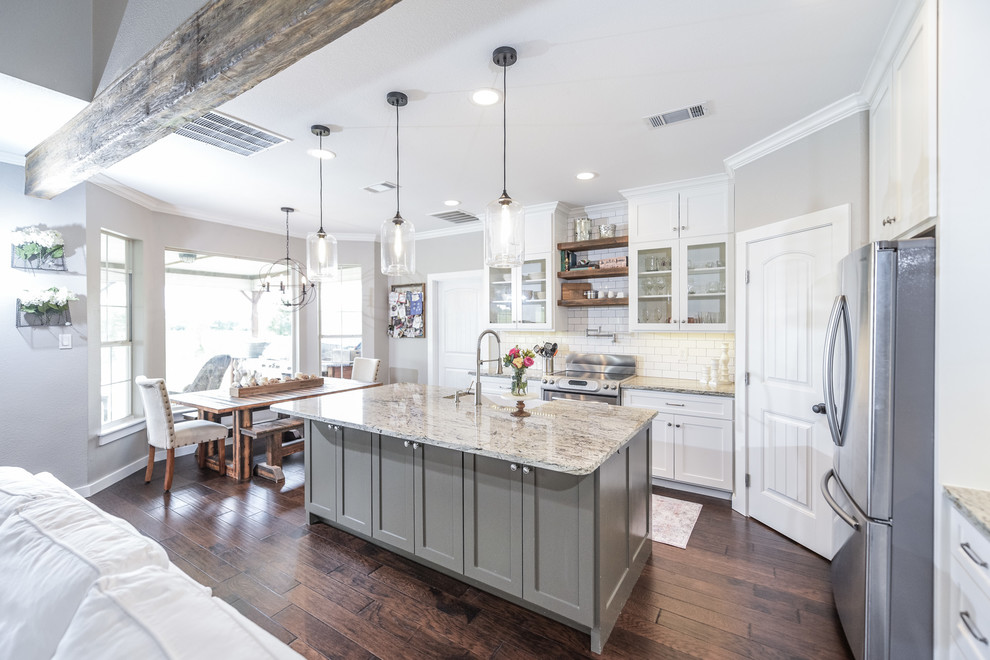 Photo of a country kitchen in Dallas with a farmhouse sink, shaker cabinets, white cabinets, granite benchtops, white splashback, ceramic splashback, stainless steel appliances, dark hardwood floors, with island and brown floor.