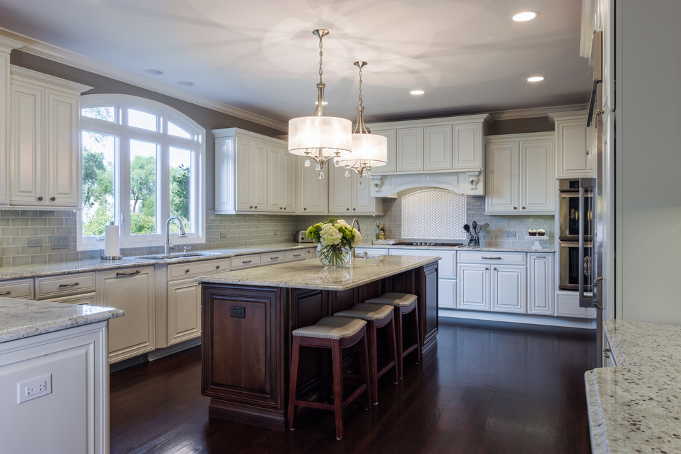 Large transitional u-shaped dark wood floor kitchen photo in Chicago with a double-bowl sink, raised-panel cabinets, white cabinets, granite countertops, gray backsplash, subway tile backsplash, stainless steel appliances and an island