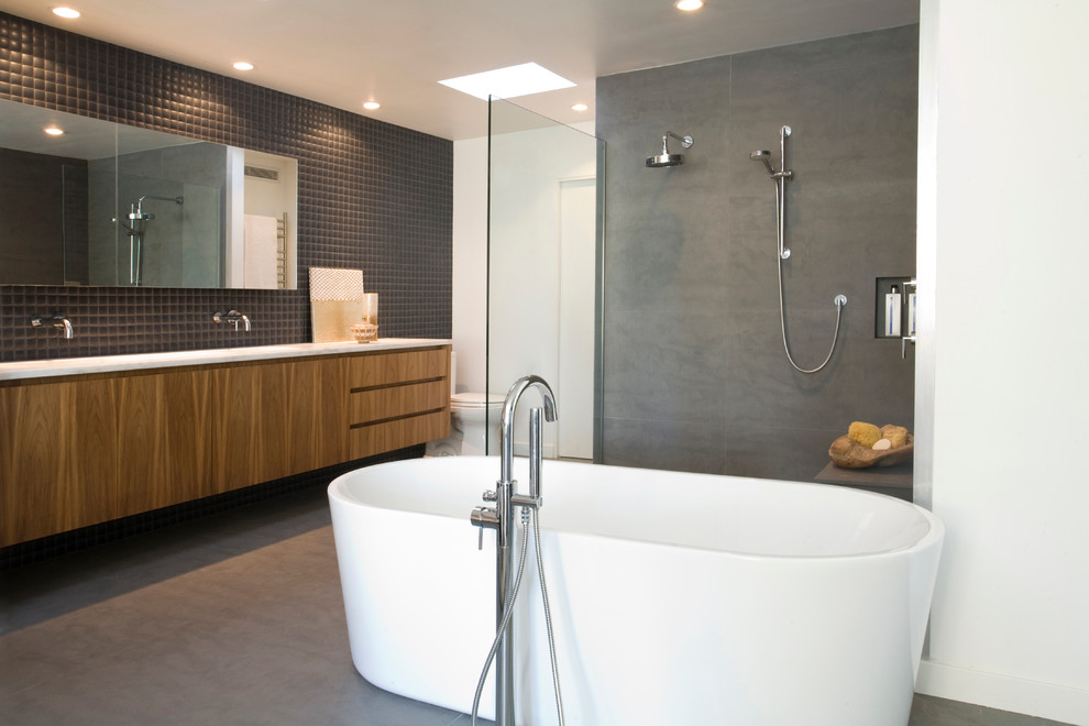 Modern bathroom in San Diego with flat-panel cabinets, medium wood cabinets, a freestanding tub and black tile.