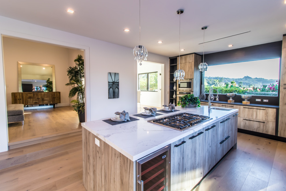 Large contemporary l-shaped eat-in kitchen in Los Angeles with a drop-in sink, flat-panel cabinets, beige cabinets, quartzite benchtops, grey splashback, window splashback, stainless steel appliances, light hardwood floors, with island, beige floor and white benchtop.