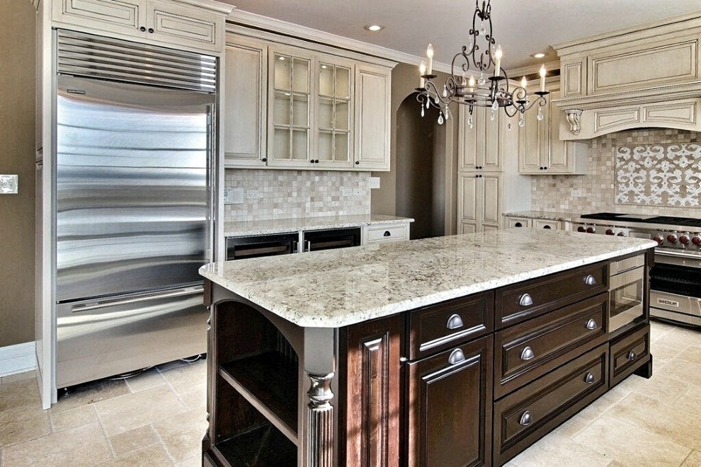 Example of a large classic l-shaped travertine floor open concept kitchen design in Chicago with a farmhouse sink, raised-panel cabinets, beige cabinets, granite countertops, beige backsplash, stone tile backsplash, stainless steel appliances and an island