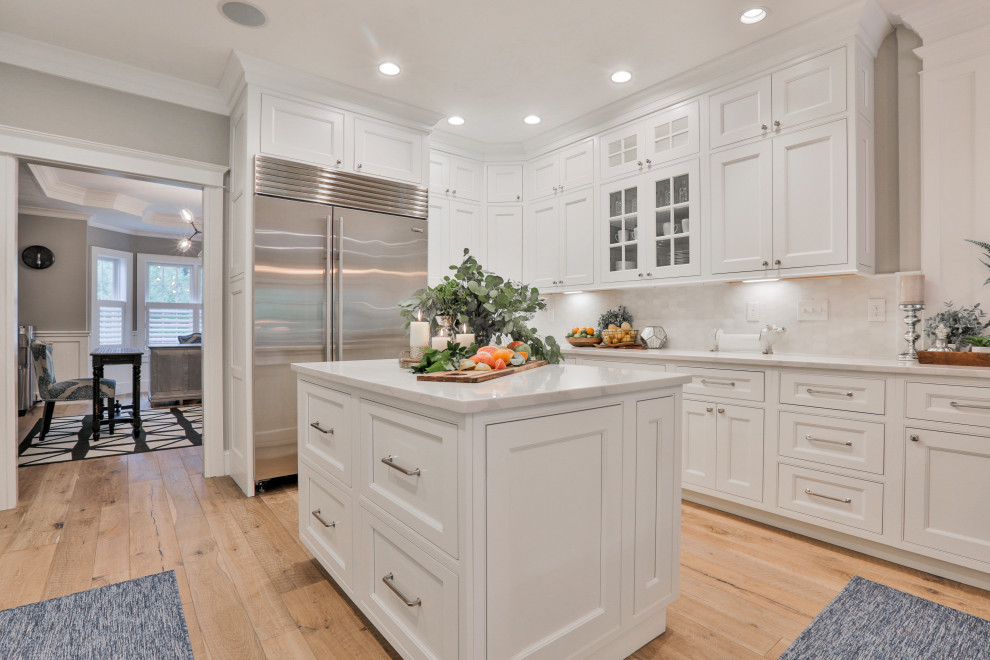 This is an example of a large traditional u-shaped eat-in kitchen in Boston with a farmhouse sink, beaded inset cabinets, white cabinets, quartz benchtops, white splashback, marble splashback, stainless steel appliances, light hardwood floors, with island, multi-coloured floor and white benchtop.