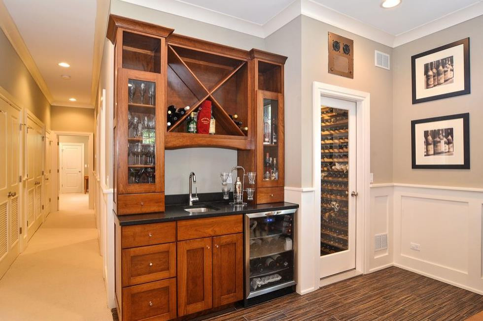 This is an example of a small traditional wet bar in Chicago with a submerged sink, shaker cabinets, brown cabinets, granite worktops, medium hardwood flooring, brown floors and black worktops.