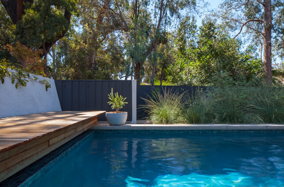 Large midcentury backyard rectangular lap pool in Los Angeles with concrete slab.
