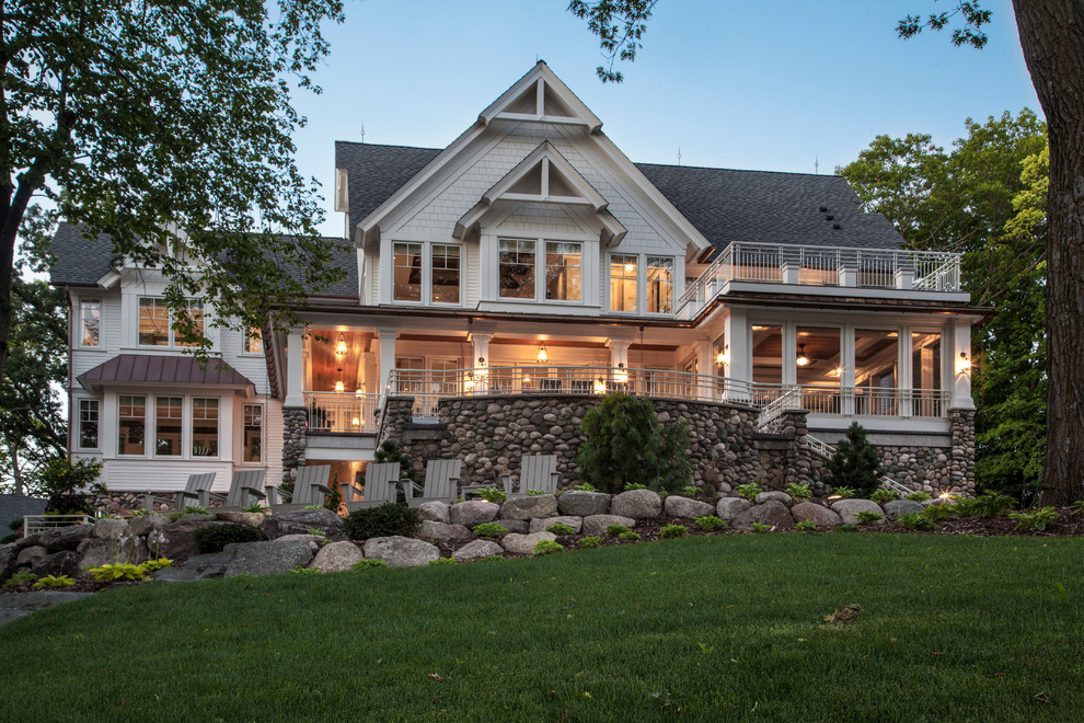 This is an example of a large country three-storey white house exterior in Minneapolis with stone veneer, a gable roof and a mixed roof.