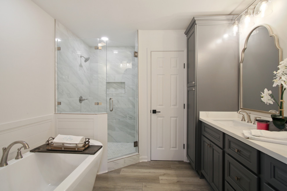 Photo of a mid-sized traditional master bathroom in New Orleans with raised-panel cabinets, blue cabinets, a freestanding tub, an open shower, a two-piece toilet, grey walls, vinyl floors, engineered quartz benchtops, a hinged shower door, white benchtops, a niche, a double vanity and a built-in vanity.