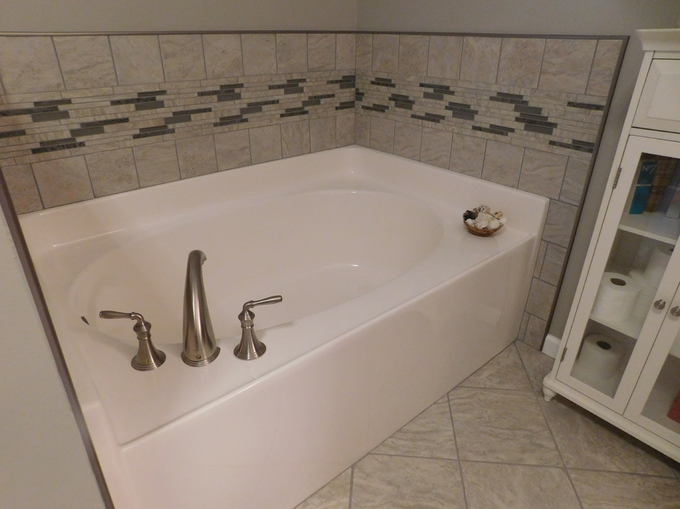 Example of a large transitional master gray tile and ceramic tile ceramic tile corner bathtub design with raised-panel cabinets, medium tone wood cabinets, a two-piece toilet, beige walls, an undermount sink and granite countertops