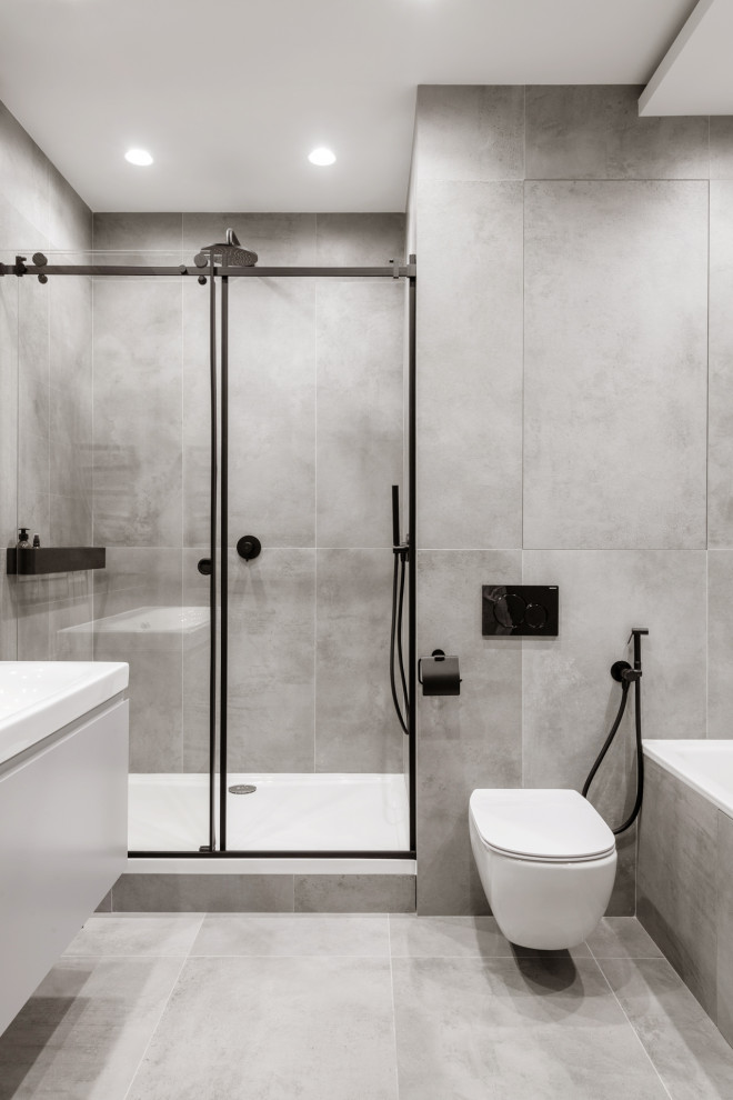 Свежая идея для дизайна: главная, серо-белая ванная комната среднего размера в современном стиле с плоскими фасадами, серыми фасадами, ванной в нише, душем в нише, инсталляцией, серой плиткой, керамогранитной плиткой, серыми стенами, полом из керамогранита, подвесной раковиной, серым полом, душем с раздвижными дверями, белой столешницей, зеркалом с подсветкой, тумбой под одну раковину и подвесной тумбой - отличное фото интерьера