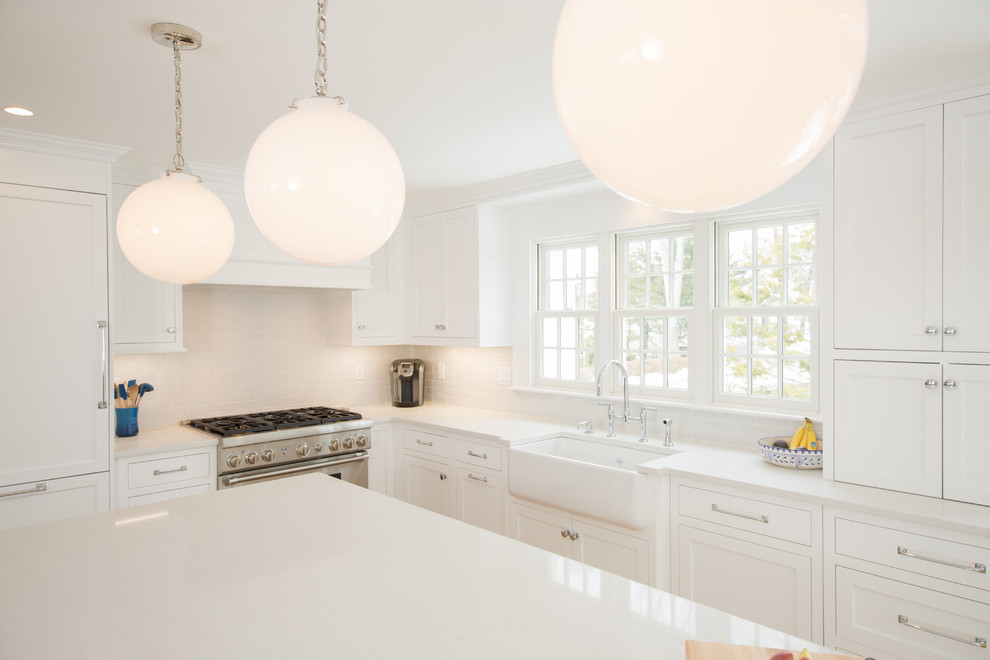 Example of a mid-sized transitional l-shaped medium tone wood floor and brown floor open concept kitchen design in Boston with a farmhouse sink, shaker cabinets, white cabinets, quartz countertops, white backsplash, subway tile backsplash, paneled appliances, an island and white countertops