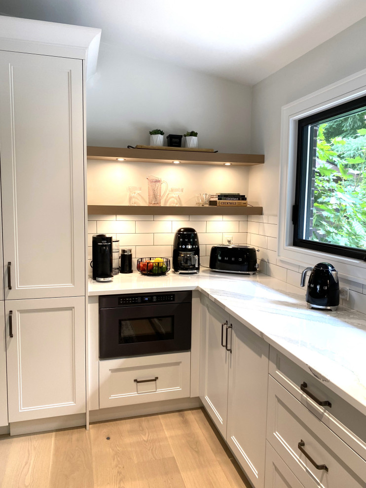 Example of a large transitional l-shaped light wood floor and vaulted ceiling open concept kitchen design in Toronto with an undermount sink, recessed-panel cabinets, white cabinets, quartz countertops, white backsplash, porcelain backsplash, stainless steel appliances, an island and white countertops