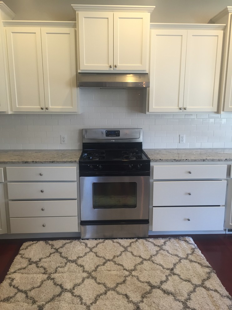 Inspiration for a mid-sized transitional single-wall dark wood floor and brown floor enclosed kitchen remodel with an undermount sink, recessed-panel cabinets, white cabinets, granite countertops, white backsplash, subway tile backsplash, stainless steel appliances and no island