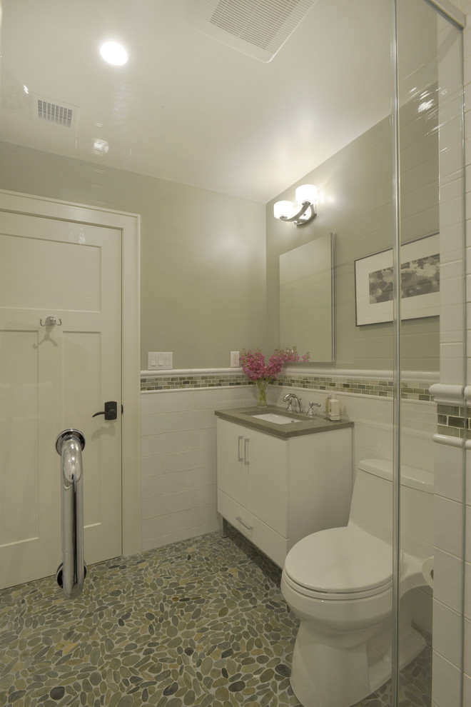 Inspiration for a mid-sized transitional 3/4 bathroom in New York with furniture-like cabinets, white cabinets, an alcove shower, a one-piece toilet, white tile, porcelain tile, grey walls, pebble tile floors, an undermount sink, soapstone benchtops, green floor and a hinged shower door.