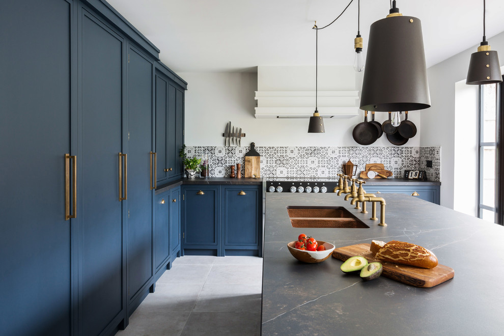 Large industrial u-shaped eat-in kitchen in Essex with a double-bowl sink, shaker cabinets, blue cabinets, solid surface benchtops, multi-coloured splashback, ceramic splashback, black appliances, porcelain floors, with island, grey floor and black benchtop.