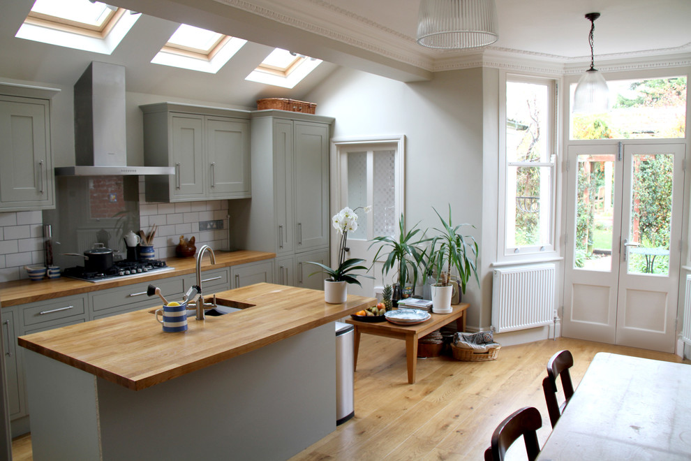 This is an example of a mid-sized contemporary eat-in kitchen in Other with recessed-panel cabinets, grey cabinets, zinc benchtops, white splashback, ceramic splashback, light hardwood floors and with island.