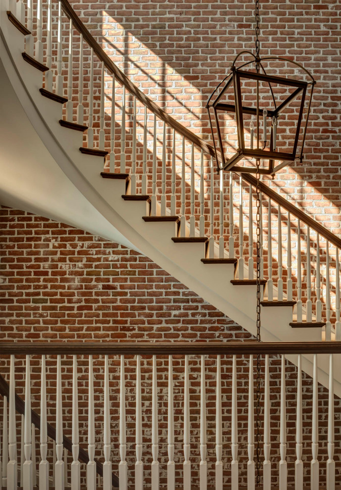 This is an example of a large traditional carpeted curved staircase in Baltimore with carpet risers, wood railing and brick walls.