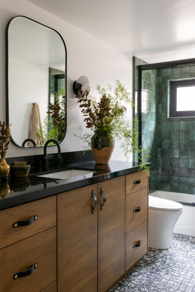 Photo of a mid-sized contemporary bathroom in Sacramento with flat-panel cabinets, an alcove tub, a shower/bathtub combo, a one-piece toilet, green tile, ceramic tile, white walls, mosaic tile floors, an undermount sink, granite benchtops, black floor, a sliding shower screen, black benchtops, a niche, a single vanity, a built-in vanity and medium wood cabinets.