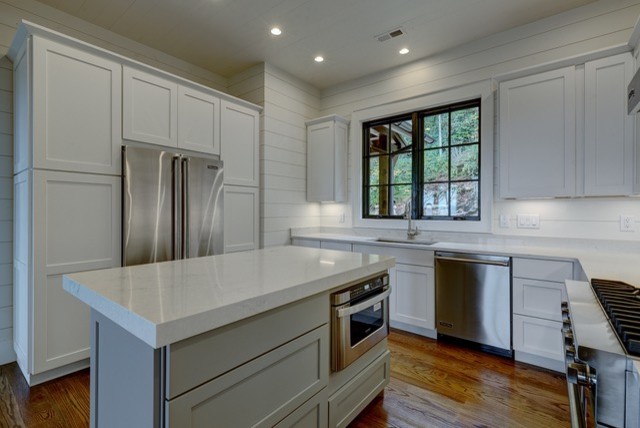 Mid-sized mountain style u-shaped medium tone wood floor and brown floor kitchen photo with an undermount sink, shaker cabinets, white cabinets, quartz countertops, white backsplash, wood backsplash, stainless steel appliances and an island