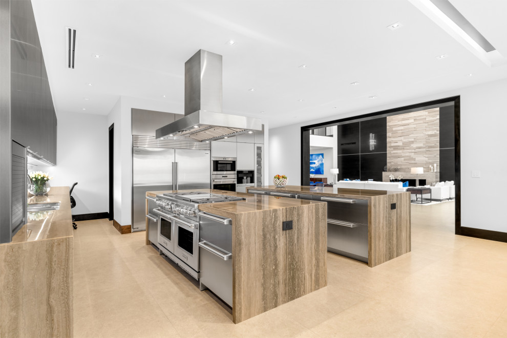 Inspiration for a large modern l-shaped open plan kitchen with a double-bowl sink, flat-panel cabinets, stainless steel cabinets, marble benchtops, stainless steel appliances, porcelain floors, multiple islands, blue floor and beige benchtop.