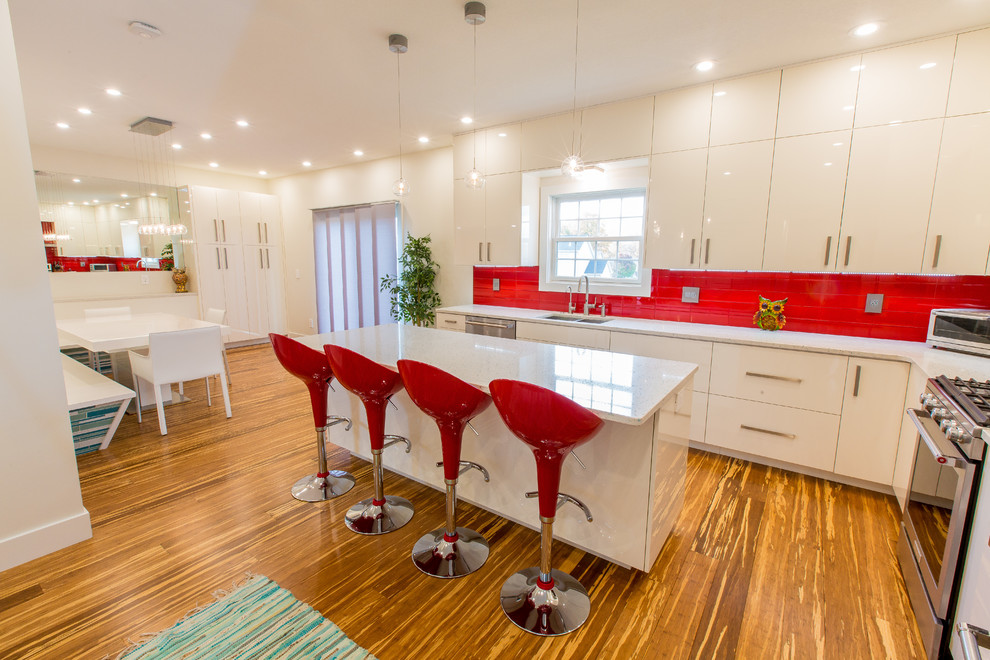 Photo of a large contemporary l-shaped eat-in kitchen in Other with an undermount sink, flat-panel cabinets, white cabinets, quartzite benchtops, red splashback, glass tile splashback, stainless steel appliances, bamboo floors, with island, brown floor and white benchtop.