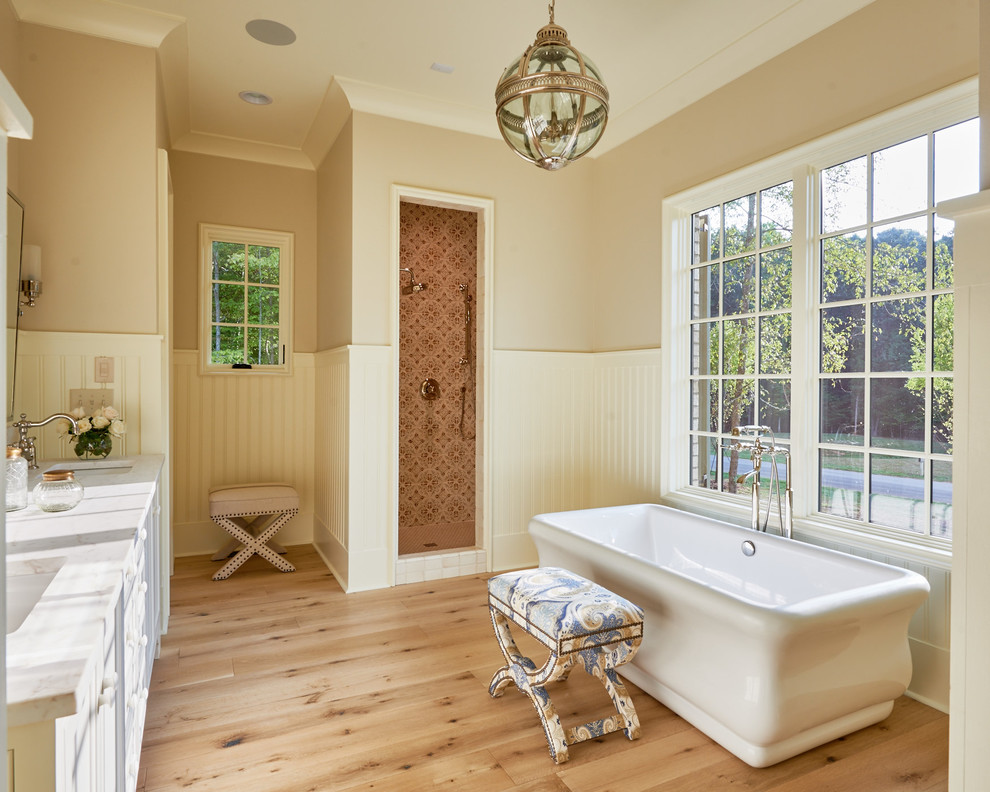 Photo of a large country master bathroom in Charlotte with an undermount sink, white cabinets, a freestanding tub, an alcove shower and light hardwood floors.