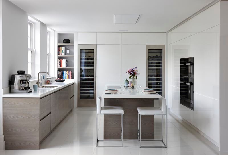 Large modern u-shaped open plan kitchen in London with an integrated sink, flat-panel cabinets, white cabinets, solid surface benchtops, panelled appliances, ceramic floors, with island, white floor and white benchtop.