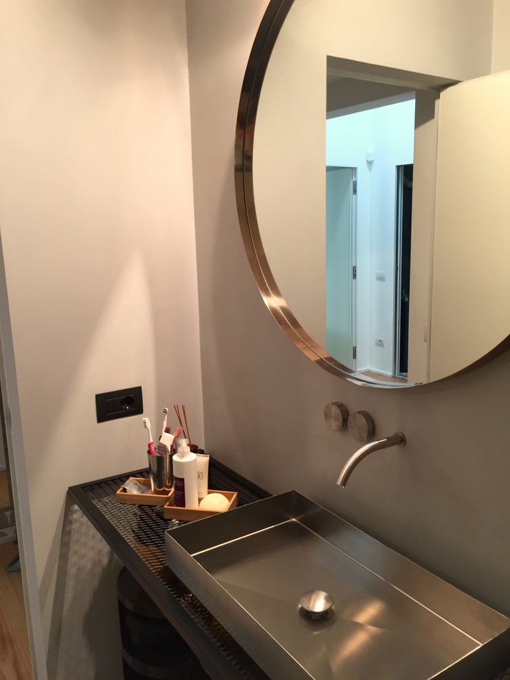 Expansive industrial 3/4 bathroom in Milan with a wall-mount toilet, porcelain floors, a vessel sink, stainless steel benchtops, grey floor, an open shower and black benchtops.