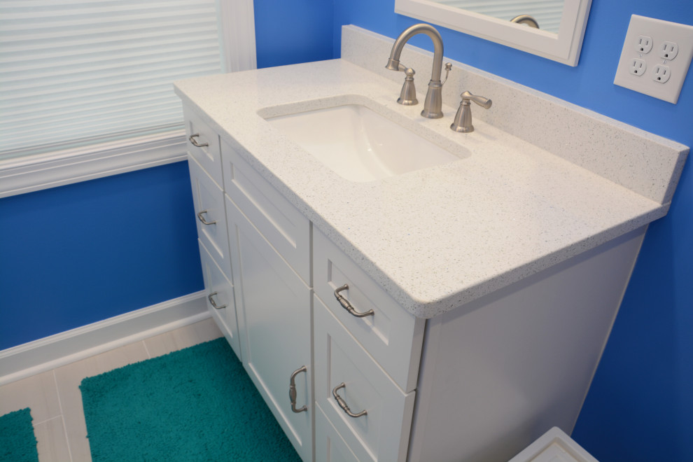 Foto på ett mellanstort maritimt vit en-suite badrum, med luckor med infälld panel, vita skåp, en hörndusch, vit kakel, blå väggar, ett undermonterad handfat, bänkskiva i kvarts, grått golv och dusch med gångjärnsdörr