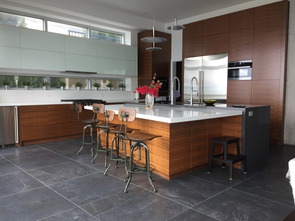 Large modern l-shaped kitchen in Vancouver with an undermount sink, flat-panel cabinets, medium wood cabinets, quartz benchtops, white splashback, glass sheet splashback, stainless steel appliances, with island and grey floor.