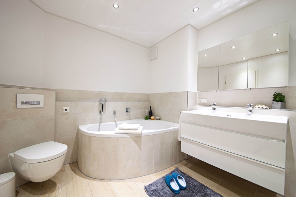 Mittelgroßes Modernes Duschbad mit flächenbündigen Schrankfronten, weißen Schränken, Eckbadewanne, Duschbadewanne, Wandtoilette, beigen Fliesen, Keramikfliesen, weißer Wandfarbe, hellem Holzboden, integriertem Waschbecken und beigem Boden in Sonstige