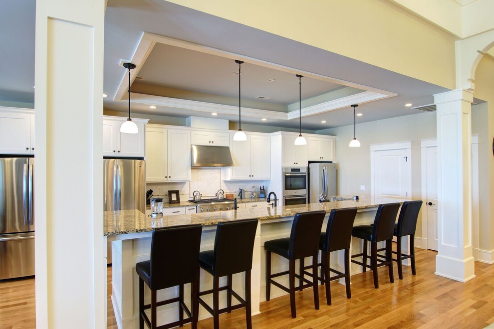 Mid-sized beach style galley medium tone wood floor eat-in kitchen photo with a double-bowl sink, shaker cabinets, white cabinets, granite countertops, white backsplash, subway tile backsplash, stainless steel appliances and an island