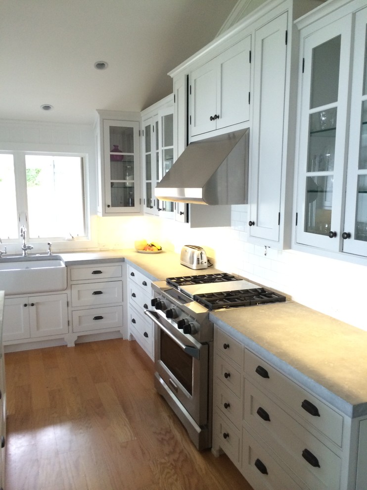 Photo of a mid-sized traditional l-shaped open plan kitchen in Richmond with a farmhouse sink, shaker cabinets, white cabinets, concrete benchtops, white splashback, porcelain splashback, stainless steel appliances, bamboo floors and with island.