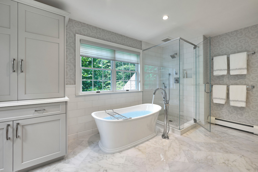 Inspiration for a mid-sized transitional master bathroom in New York with shaker cabinets, grey cabinets, a freestanding tub, a corner shower, white tile, porcelain tile, grey walls, marble floors, an undermount sink, solid surface benchtops, white floor and a hinged shower door.
