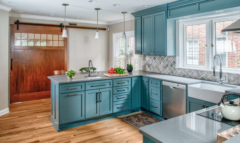 Inspiration for a mid-sized craftsman u-shaped medium tone wood floor and brown floor enclosed kitchen remodel in Indianapolis with a farmhouse sink, shaker cabinets, blue cabinets, quartz countertops, beige backsplash, ceramic backsplash, stainless steel appliances and a peninsula
