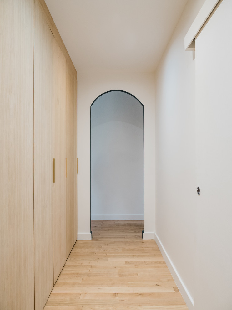 Large modern gender-neutral walk-in wardrobe in Paris with recessed-panel cabinets, light wood cabinets, light hardwood floors and brown floor.