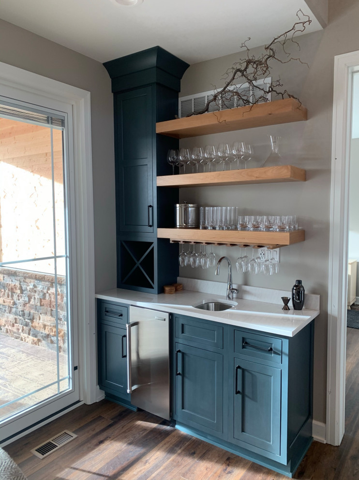 This is an example of a small country single-wall wet bar in Other with an undermount sink, shaker cabinets, blue cabinets, quartz benchtops, vinyl floors, brown floor and white benchtop.
