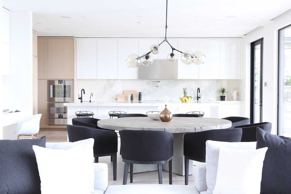 Large modern l-shaped open plan kitchen in Vancouver with an undermount sink, flat-panel cabinets, white cabinets, marble benchtops, white splashback, marble splashback, panelled appliances, medium hardwood floors, with island, white floor and white benchtop.