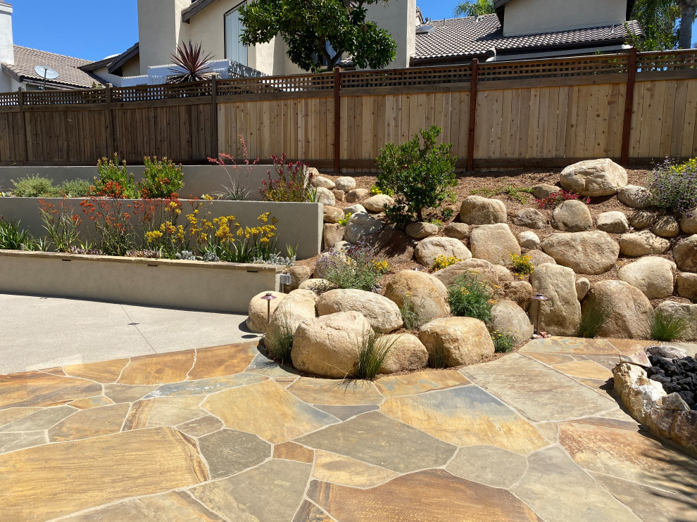 This is an example of a large mediterranean sloped full sun xeriscape for summer in San Diego with a retaining wall and natural stone pavers.
